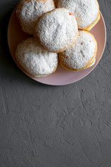 Homemade sweet donuts with powdered sugar on pink plate over concrete background, top view. Space for text.