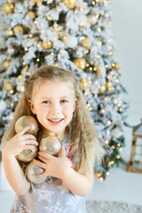 girl decorating christmas tree with balls at home. winter holidays and people concept