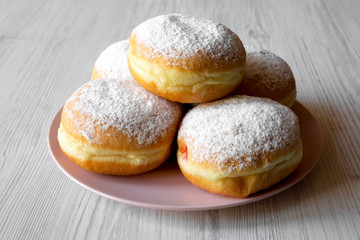 Naklejka na ściany i meble Homemade sweet donuts with powdered sugar on pink plate on white wooden table, side view. Closeup.