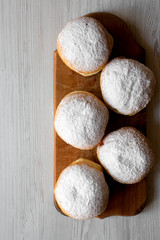 Homemade sweet donuts with jelly and powdered sugar on rustic wooden board over white wooden background, overhead view. Copy space.