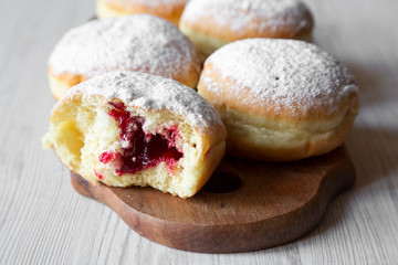Homemade donuts with jelly and powdered sugar on wooden board on white wooden background, side view.