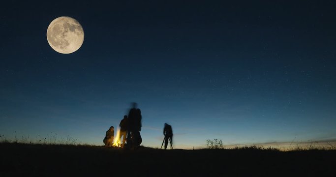 Long low angle timelapse shot of friends stargazing together and looking on big moon using a professional telescope at night