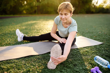 Mature woman practicing yoga outdoor exercise or doing fitness.