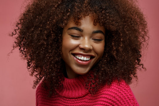 Portrait of a young African American afro woman in pink studio smiling of joy with eyes closed