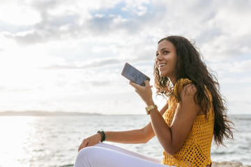 Young woman sending a voice message with her smartphone on the b
