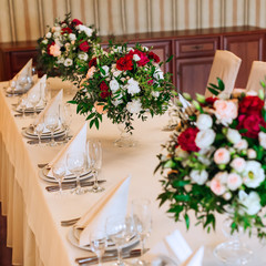 a close-up of a table with a white tablecloth on which cutlery, plates with napkins and glasses. beautiful bouquets in transparent vases