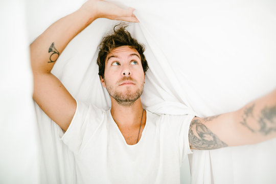 portrait of a tattoed youn man under the sheets