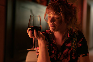Beautiful ginger girl drinking a glass of red wine near a fire pit