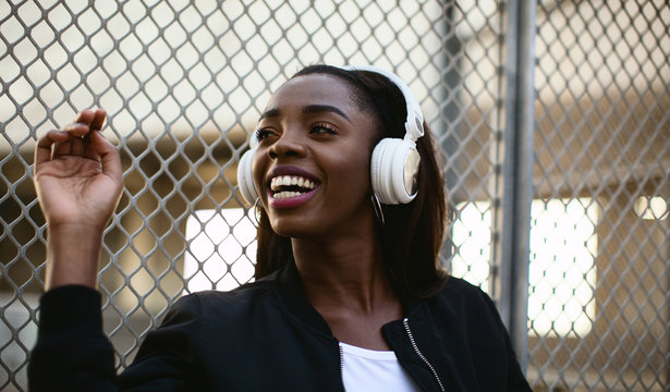 Portrait of a cool young woman listening music on headphones standing on the street.