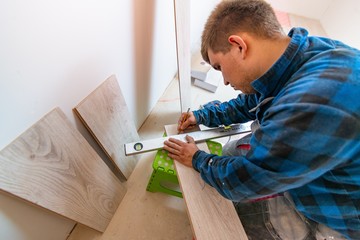 Man measuring and marking laminate floor tile for cutting, installing laminate flooring.