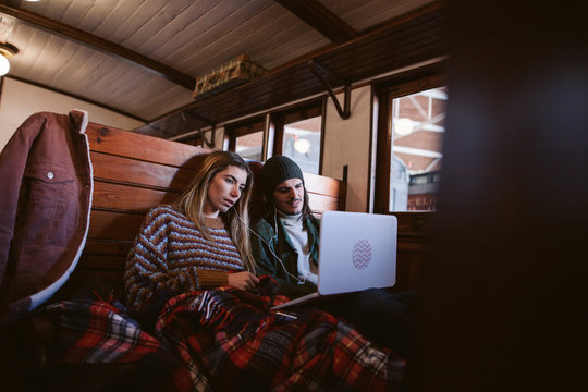 Young couple using laptop traveling by wooden train.