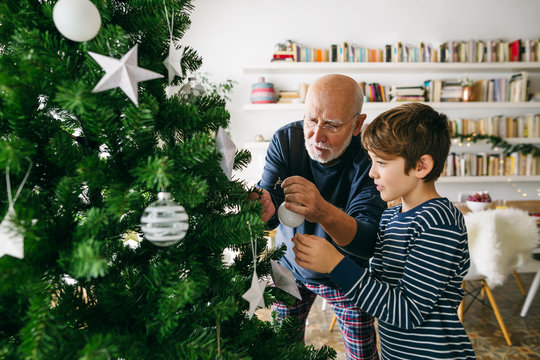 Grandpa and little boy decorating Christmas tree. Family celebrating Christmas at home.