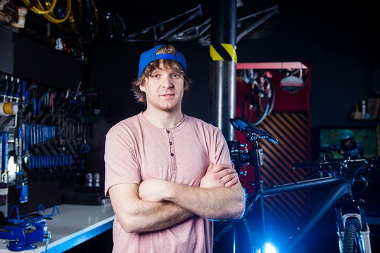 Small business and bicycle transport service. Portrait of a young man in a cap posing against the backdrop of a bicycle workshop and a tool for setting up and repairing