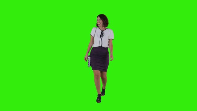 Stylish happy woman walking and smiling over a green screen in a full frontal shot.