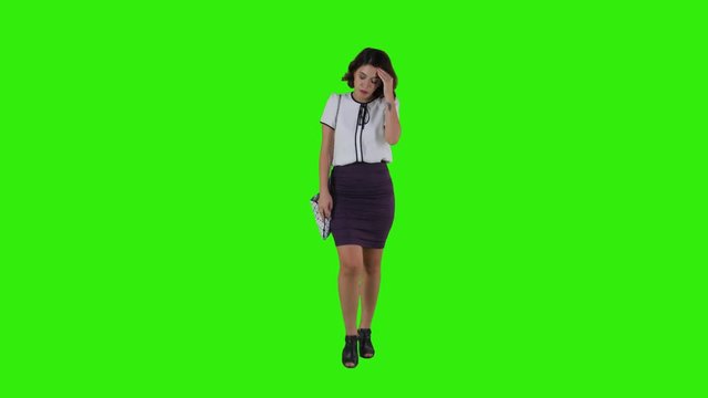 Stylish sad woman walking while having a headache over a green screen in a full frontal shot.