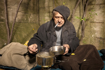 Ugly pauper man living outdoor preparing and eating lentil soup