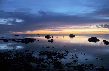 Calm water at twilight with boulders along a rocky shore