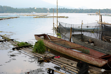 Obraz premium Dilapidated, rusty boats beside bamboo raft on dirty lake contributing to water pollution