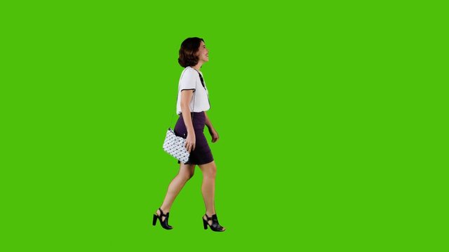 Stylish happy woman walking and smiling over a green screen in a full side shot.