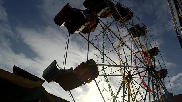 People are content riding on cheap, dilapidated and rustic ferris wheel ride in a small town festivity. silhouettes