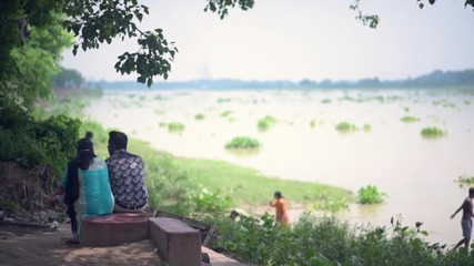 Romantic Indian couple in love sit at Ganga or Ganges river bank, people bathing in river