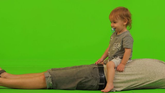 A dad plays with his cute toddler son over a green screen, medium long shot.