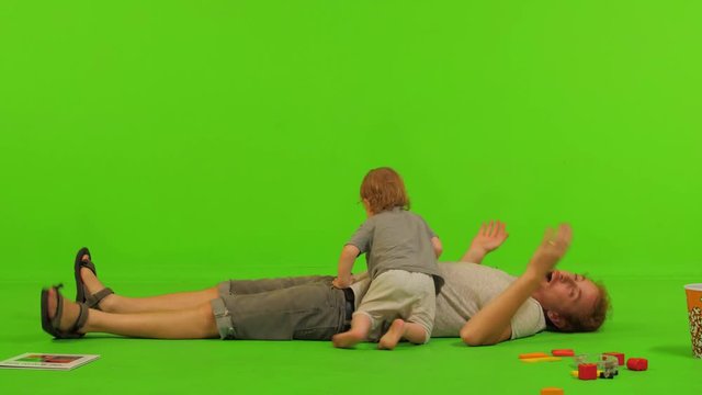 A dad plays with his cute toddler son over a green screen, full long shot.
