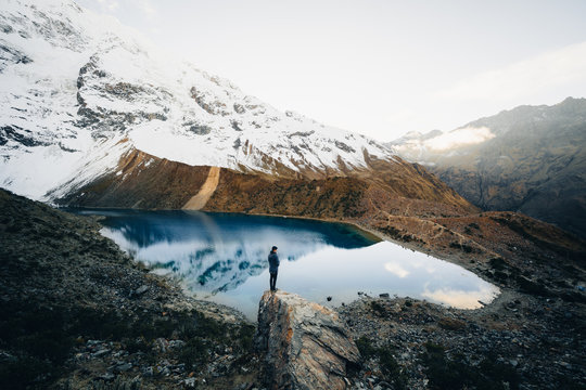 Hiker standing on rock overlooking blue alpine lake, New Zealand