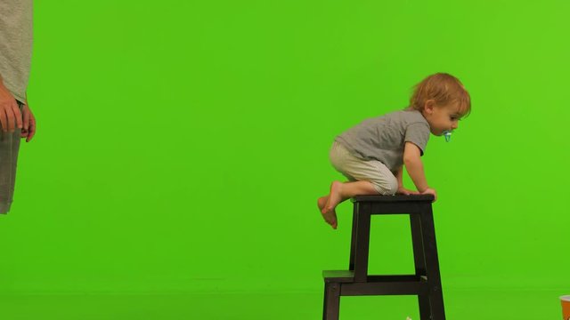 A  beautiful toddler climbs a small stool over a green screen, going up and down.