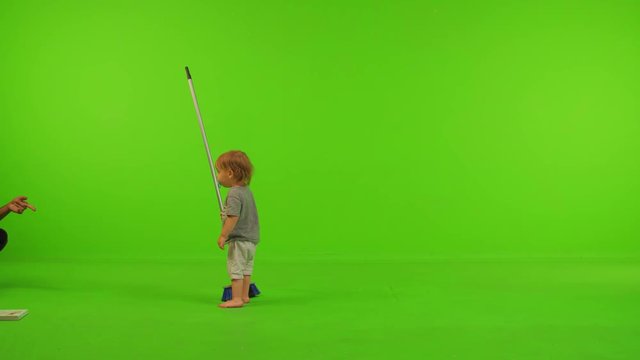 A toddler plays and walk with a broom happily over a green screen.