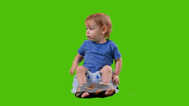 Cute little toddler sits on a potty, points and nods his heading a full shot over a green screen.