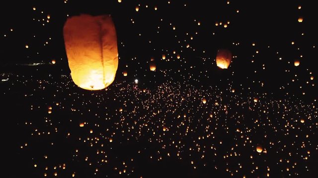 Drone shot of thousands of glowing lanterns flying across screen. Beautiful floating lanterns light the night sky as thousands of people gather throw fire lanterns in the sky.
