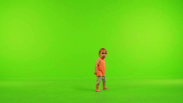 Cute little toddler walks happily from side to side, stops and eat in a full shot over a green screen.