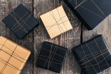 Six gifts wrapped in black and gold on wooden surface