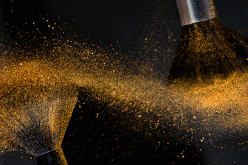 Make-up brushes with golden face powder against dark background