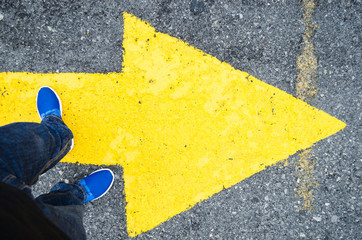 close up on the legs of a man standing on a yellow arrow in the direction to the right, concept of decisions in life.