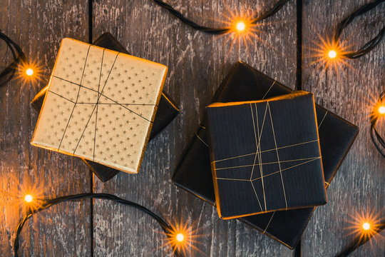 Four gifts on wooden surface surrounded by christmas lights