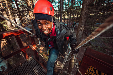 Young man has a big smile while climbing a rope bridge during an outdoor zip line course