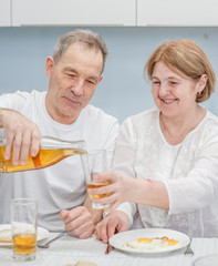 Obraz na płótnie Canvas an elderly man pours juice for breakfast to his wife