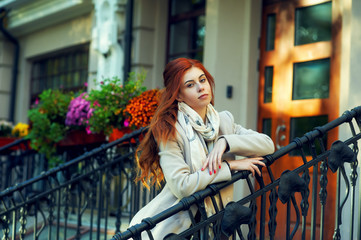Portrait of a young beautiful red-haired girl in the autumn city . Woman wearing a coat and a green dress