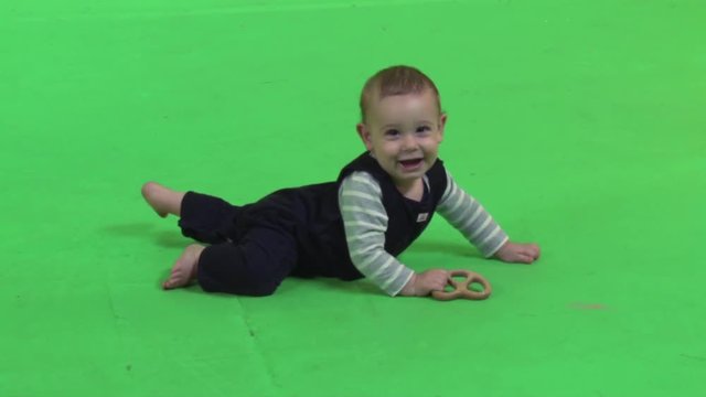 Playful baby holds a wooden pretzel happily while laughing over a green screen.