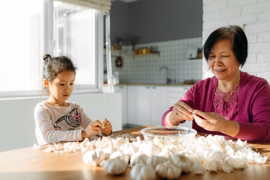 Adorable girl and her grandmother peeling garlic