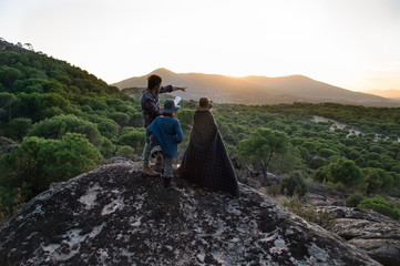 Two boys and his father sitting on a stone watching the sunset while his dad points the horizon