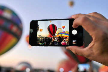 Person taking a photo with a cell phone at a hot air balloon liftoff