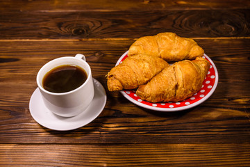 Cup of dark coffee and croissants on wooden table