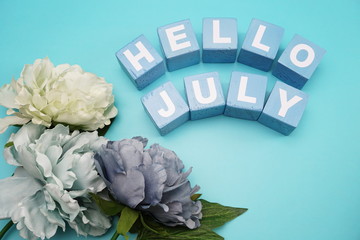 hello july with artificial peony flower on blue background