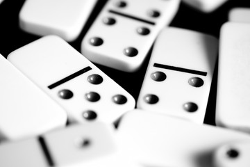 Dominoes are scattered on a dark surface close up. Black and white