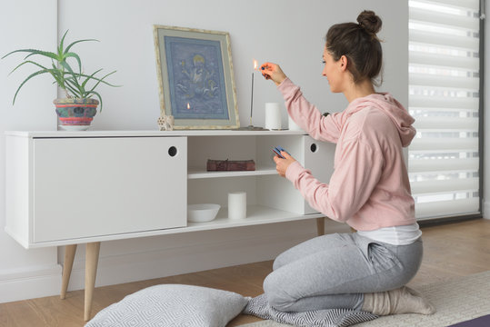 Woman lighting up a scented stick in fornt of Buddhist picture
