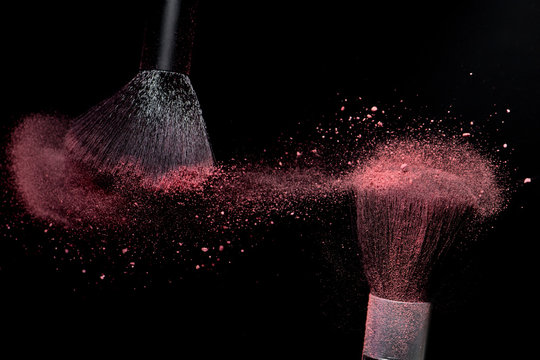 Make-up brushes with pink face powder against dark background