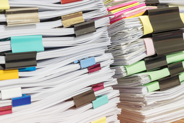 Close up pile of unfinished homework assignment stacked in archive with colorful paper clips on teacher's table waiting to be managed and inspected. Stack of paperwork. Education and business concept.